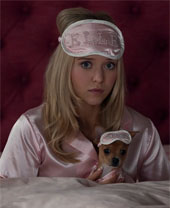 Lexi Minetree as Elle. She is in bed wearing a sleep mask pulled up so she can see and her chihuahua is wearing the same thing