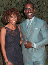Sterling K. Brown and his wife Ryan Michelle Bathe. He is wearing an iridescent blue suit and she is in a sleeveless v-neck lace dress, they are both smiling