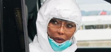 Naomi Campbell is traveling in a full hazmat suit with gloves, goggles & a mask
